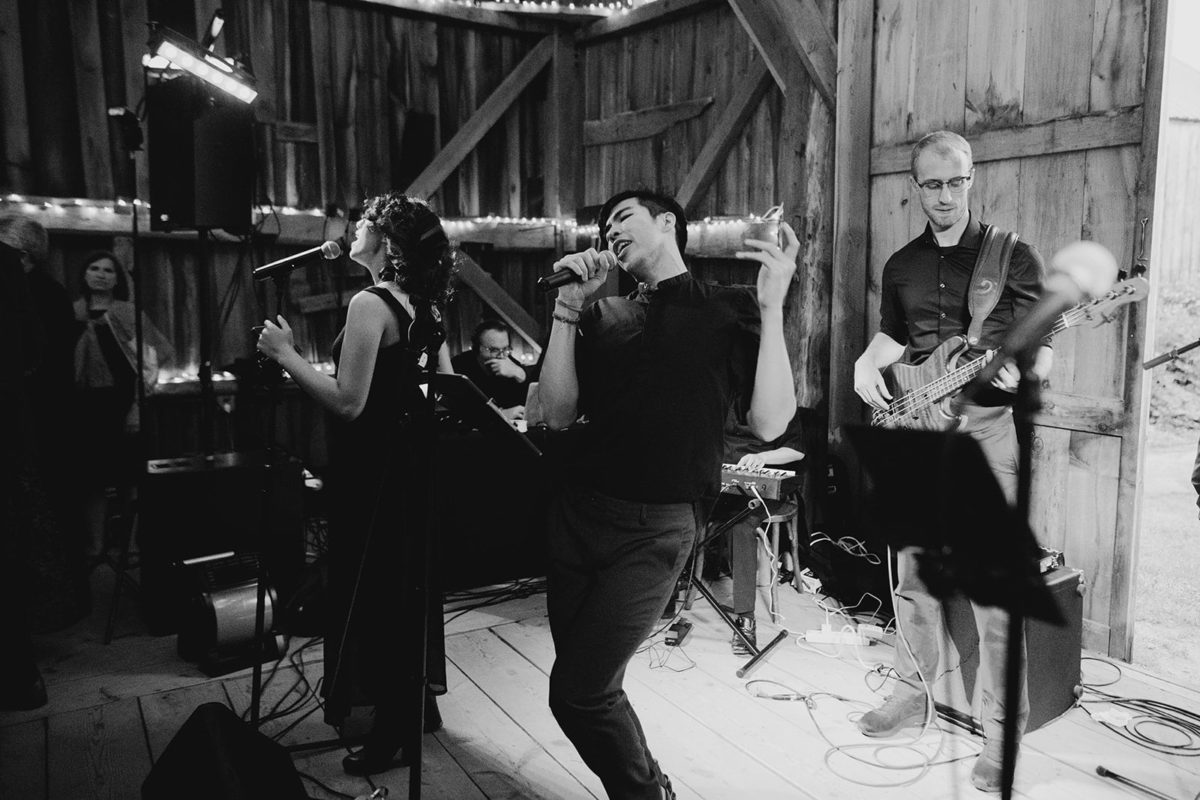 Live band performing at rustic barn wedding with passionate singers and warm string lights.
