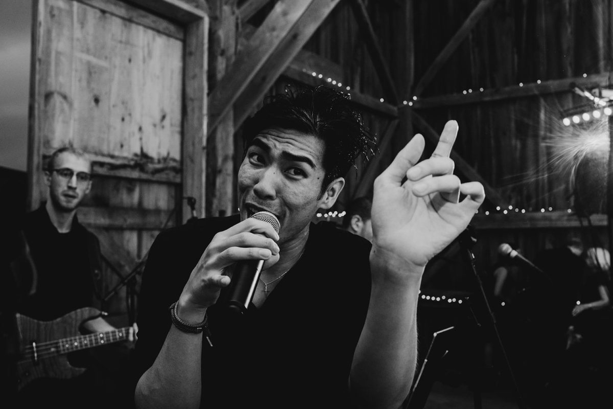 Black-and-white photo of passionate singer performing live in a rustic barn with band and lights.