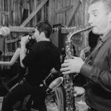 Black-and-white photo of a lively band performing in a rustic barn with warm string lights.