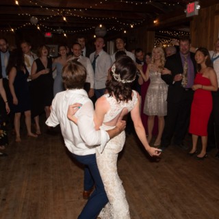 Bride and groom dancing joyfully under string lights surrounded by cheering wedding guests