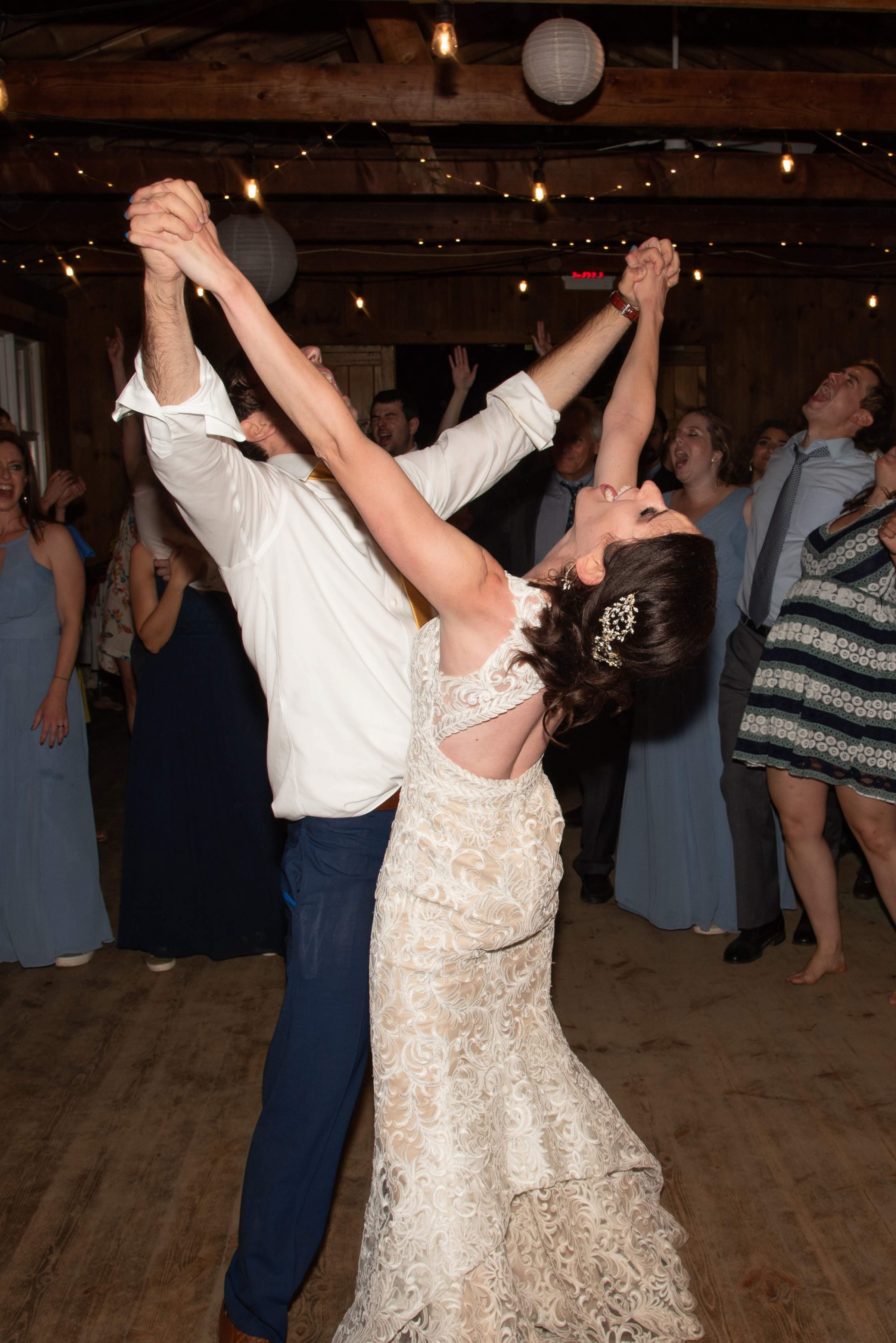 Bride and groom dancing joyfully under string lights at rustic Chequessett Country Club wedding.
