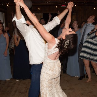 Bride and groom dancing joyfully under string lights at rustic Chequessett Country Club wedding.