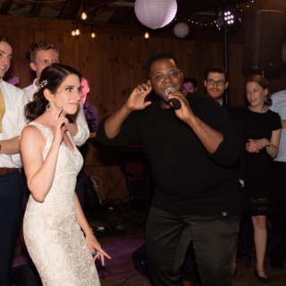 Bride enjoying live music performance at rustic wedding reception under warm lights and paper lanterns.