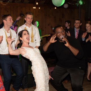 Bride dancing and singing joyfully with guests at a lively rustic wedding reception.