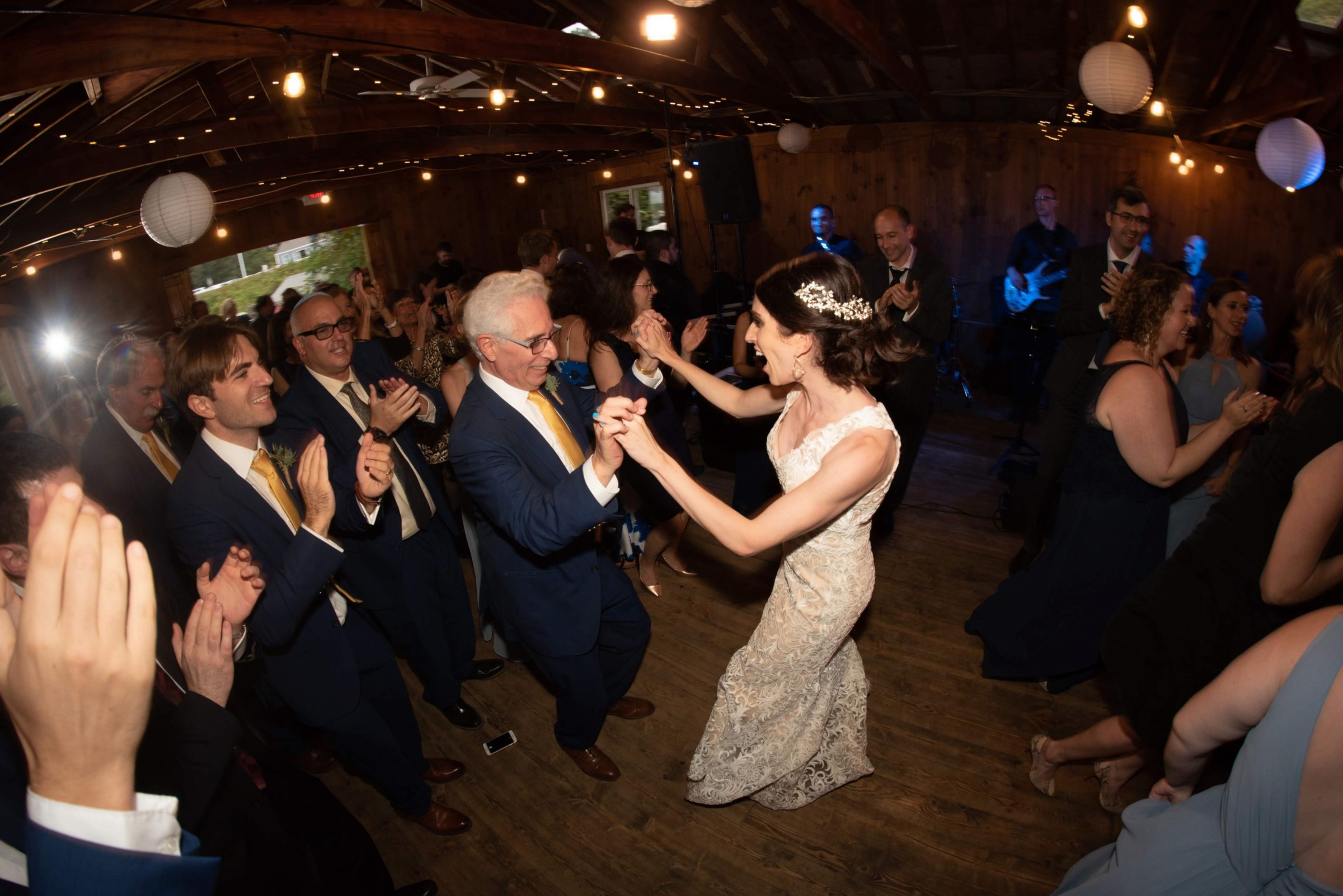 Bride dancing with older gentleman at rustic Chequessett Club wedding under warm string lights.