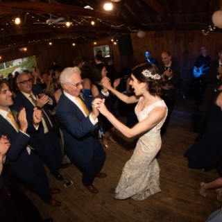 Bride dancing with older gentleman at rustic Chequessett Club wedding under warm string lights.