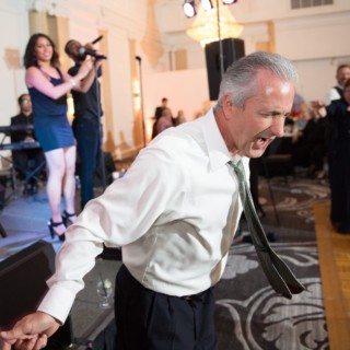 Man dancing joyfully at Boston wedding reception with live band and elegant ballroom setting.