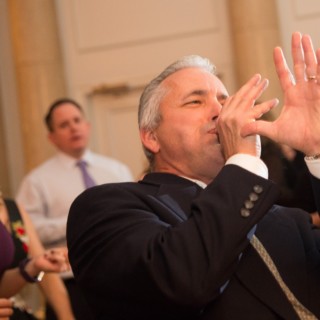 Smiling wedding guest playfully entertains crowd at elegant Boston reception under warm golden lighting.