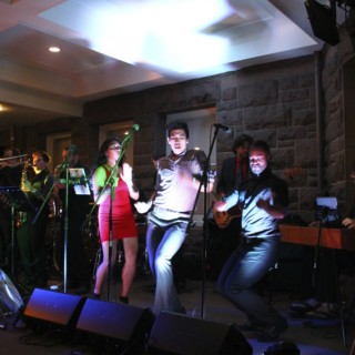Energetic live wedding band performing indoors in Newport, Rhode Island with vibrant lighting and joyful music.