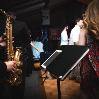Guests dancing to live jazz with saxophonist at rustic Vermont wedding reception.