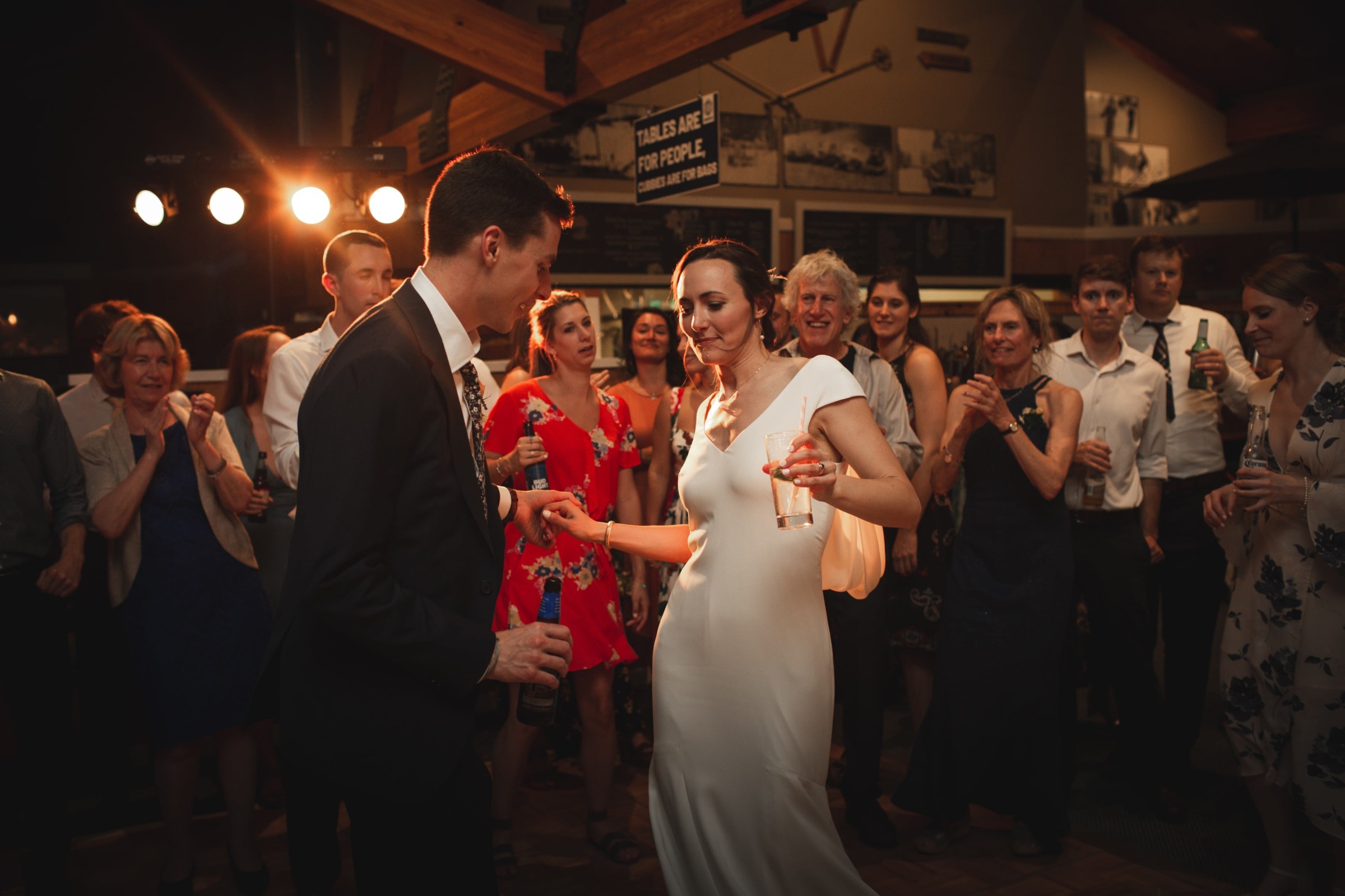 Bride and groom dancing joyfully at rustic Vermont wedding surrounded by cheering guests and warm light.
