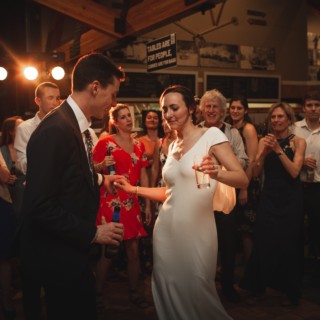 Bride and groom dancing joyfully at rustic Vermont wedding surrounded by cheering guests and warm light.