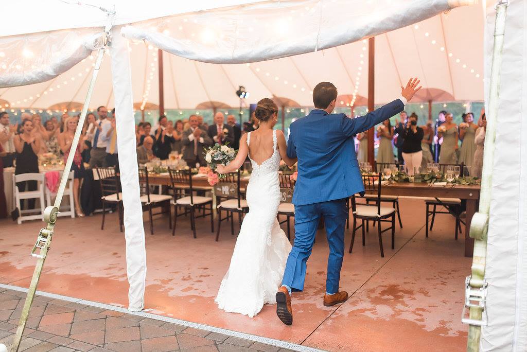Newlyweds enter glowing wedding tent at Willowdale Estate, greeted by cheering guests and romantic lights.