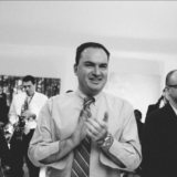 Guests clapping and smiling to live music at a joyful black-and-white wedding celebration.