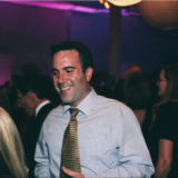 Smiling man enjoying a lively Boston wedding reception with colorful evening lighting.