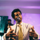 Passionate singer performing live under colorful stage lights at Boston art event.