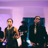 Soulful live band performing at a Boston wedding under warm pink and purple stage lighting.
