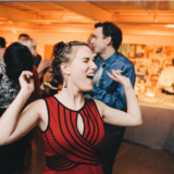 Joyful woman dancing at lively Boston wedding reception in warm golden lighting.