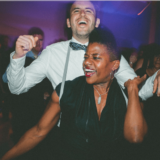 Laughing couple dancing at vibrant Boston wedding reception with colorful party lights.