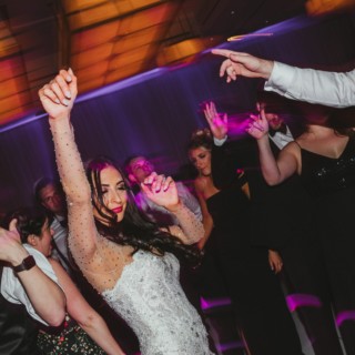 Bride dancing joyfully with guests under vibrant purple and gold lights at Boston wedding reception.