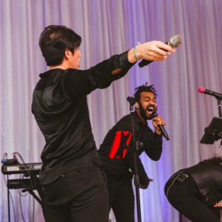 Energetic live band performing at Boston event under purple lighting with enthusiastic singers on stage.