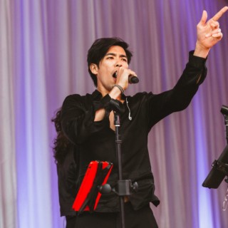 Male singer performing passionately on stage under purple lighting at elegant Boston event.
