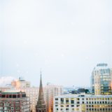 Historic church spire amid modern Boston skyline at dusk under a hazy blue evening sky.