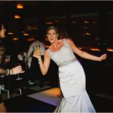 Bride dancing joyfully at Taj Boston wedding reception with guests under warm evening lights.
