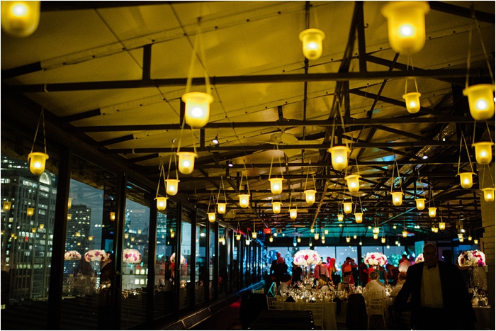 Romantic rooftop wedding reception with golden lanterns, city skyline views, and elegant floral decor.