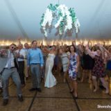 Bride and guests dancing joyfully under floral tent lights at Pelham House wedding Dennis Port.