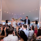 Bride and groom lifted on chairs during joyful Pelham House wedding celebration under glowing string lights.