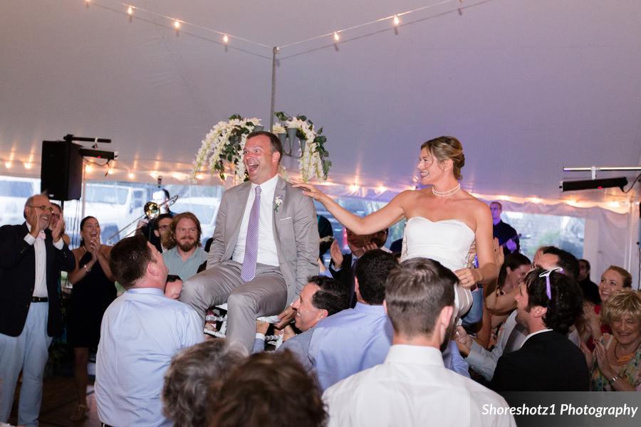 Bride and groom lifted during joyful hora dance at Pelham House wedding in Dennis Port, MA.