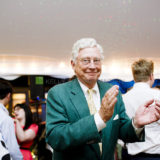 Elderly man smiling and clapping at elegant indoor wedding celebration in Westerly, Rhode Island.