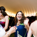 Women laughing and dancing under warm string lights at a joyful wedding celebration.