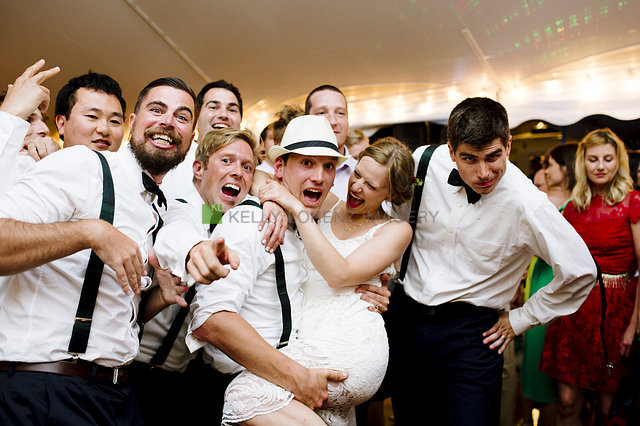 Bride laughing as groomsmen lift her during lively Rhode Island wedding celebration.