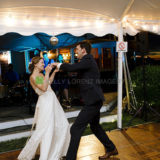 Bride and groom share a joyful first dance under glowing string lights at a romantic wedding tent.