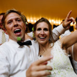 Bride and groom celebrating joyfully under glowing string lights at their evening wedding reception.