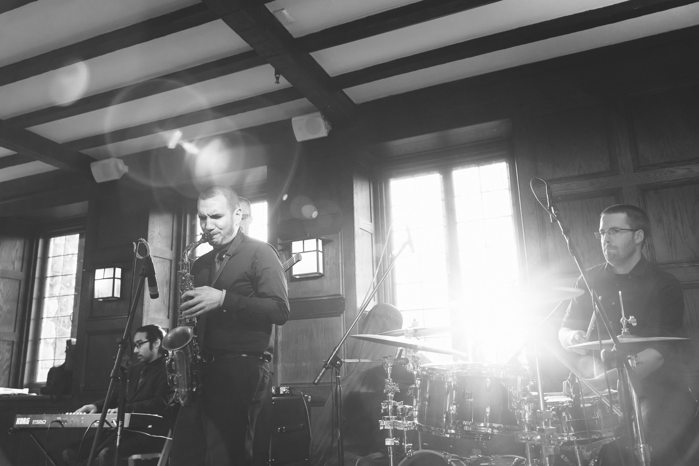 Black and white jazz trio performing live indoors with sunlight streaming through tall windows.