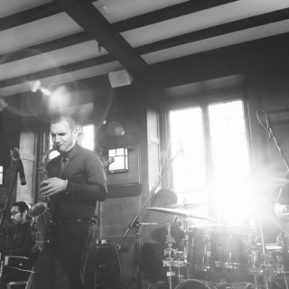 Black and white jazz trio performing live indoors with sunlight streaming through tall windows.