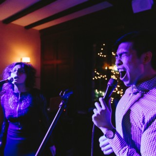 Emotional duet performance under vibrant purple and blue stage lights in a cozy indoor venue.
