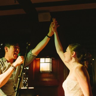 Bride and singer share a joyful high-five during warm, golden-lit Willowdale Estate wedding celebration.