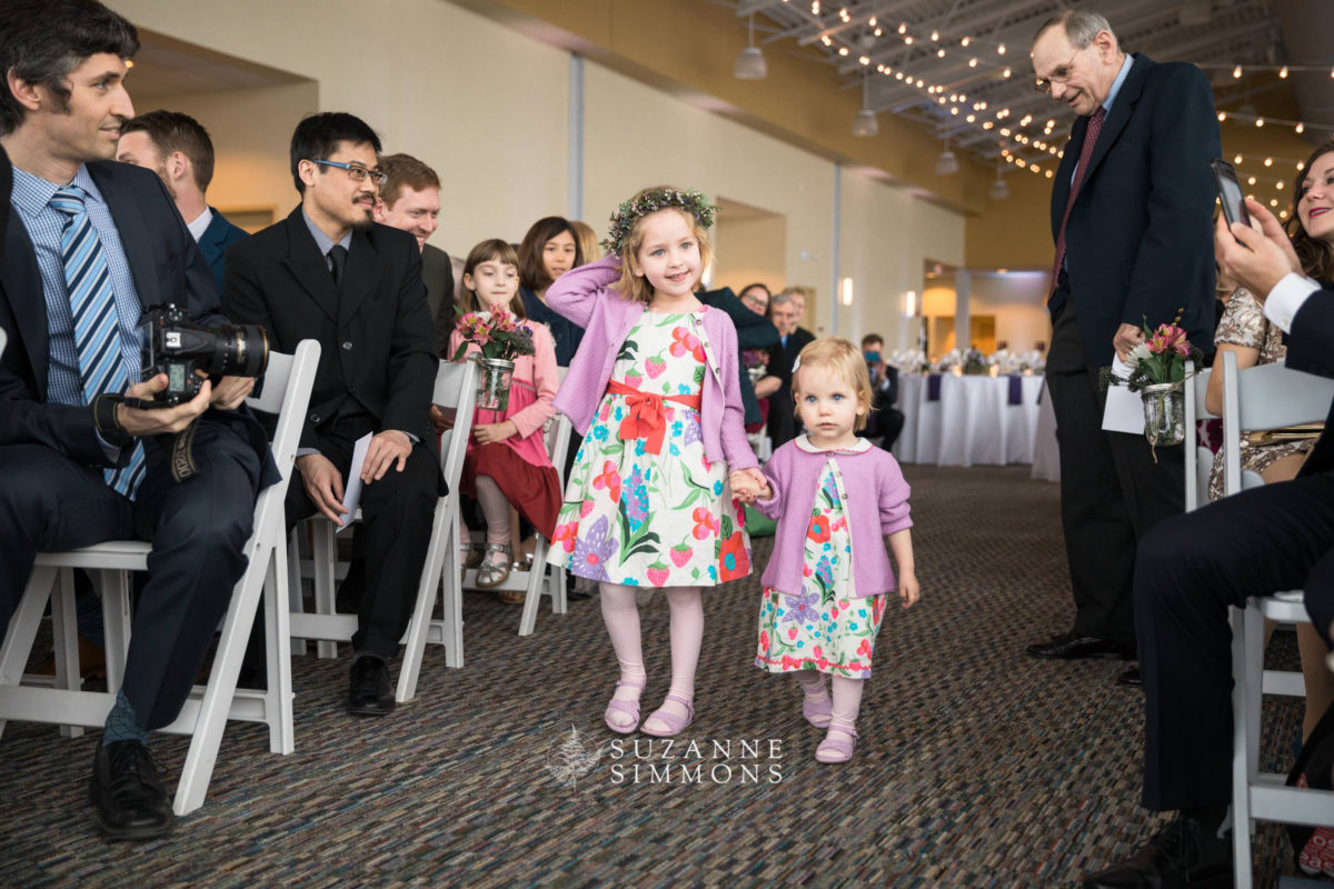 Flower girls walking down the aisle at a Portland wedding surrounded by smiling guests.