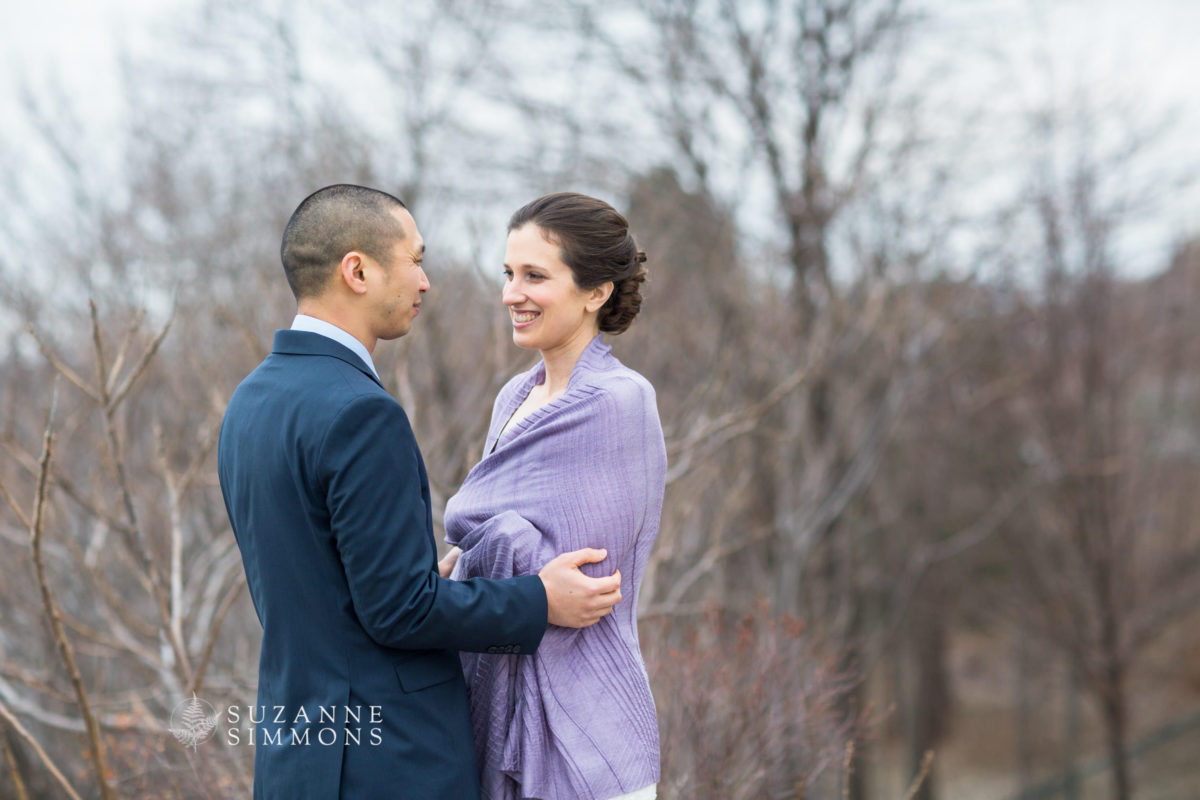 Romantic couple embracing outdoors amid bare trees in soft early spring light.