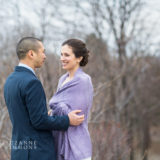 Romantic couple embracing outdoors amid bare trees in soft early spring light.