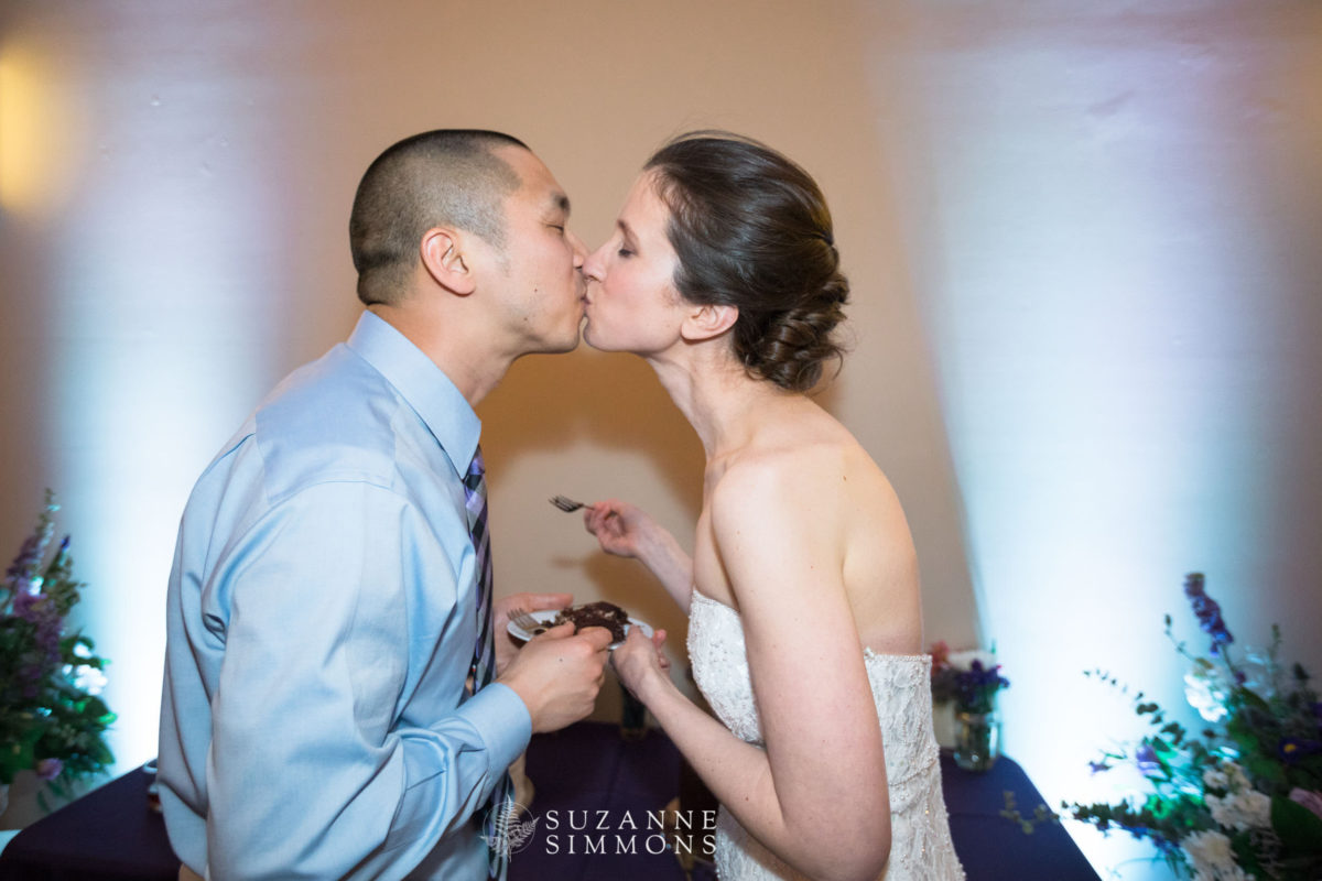 Bride and groom share a romantic cake-cutting kiss at their Ocean Gateway wedding in Portland.