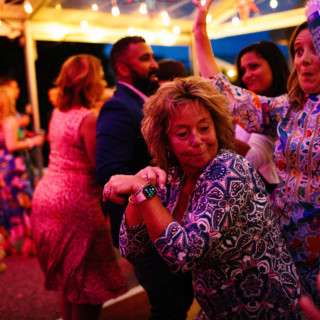 Guests dancing joyfully under warm string lights at an outdoor Maine wedding celebration.