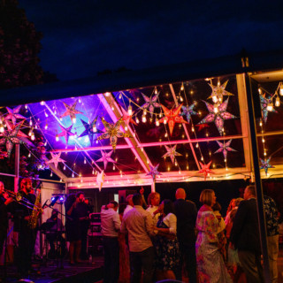 Colorful outdoor wedding celebration with live band, dancing guests, and glowing star lanterns at night.