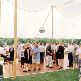 Guests dancing under white canopy tent with string lights at elegant outdoor wedding reception.