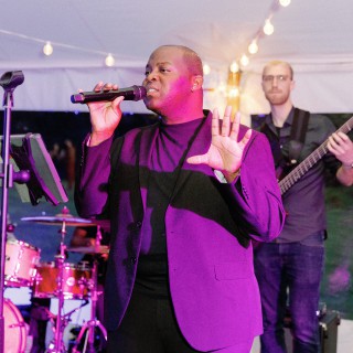 Lead singer and bassist perform live under string lights at a vibrant wedding reception.