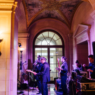 Live band performing in ornate historic ballroom with golden lighting and elegant architectural details.